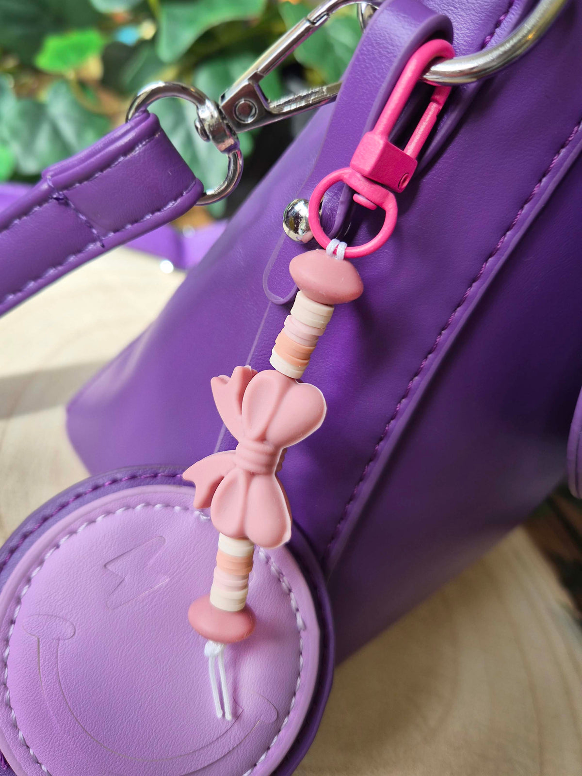 Dusty pink bow keychain on a purple bag.