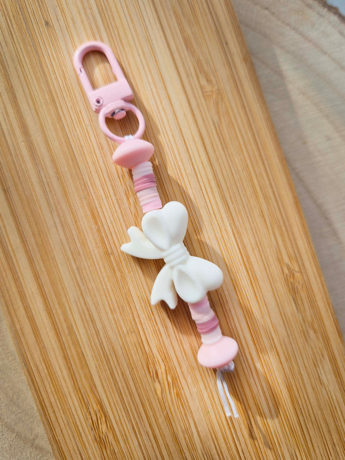White bow keychain on wooden board.