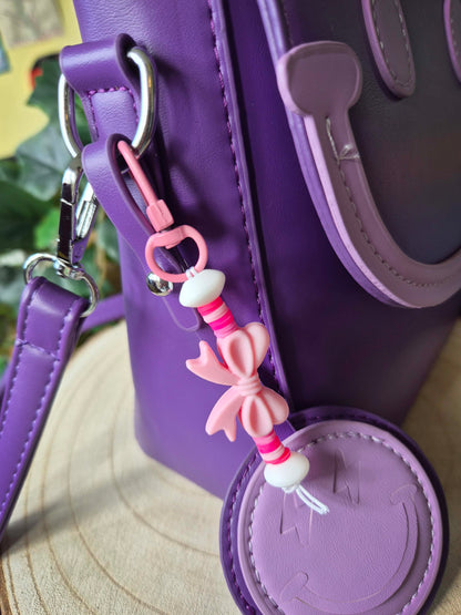 Light pink bow keychain clipped to a purple school bag zip