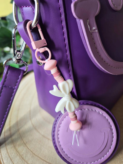 White bow keychain on a purple bag.