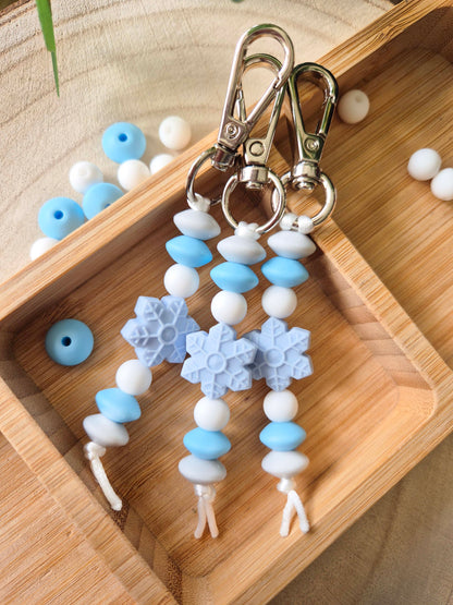Frosty snowflake keyrings with light blue and white beads and silver clasps on a wooden tray