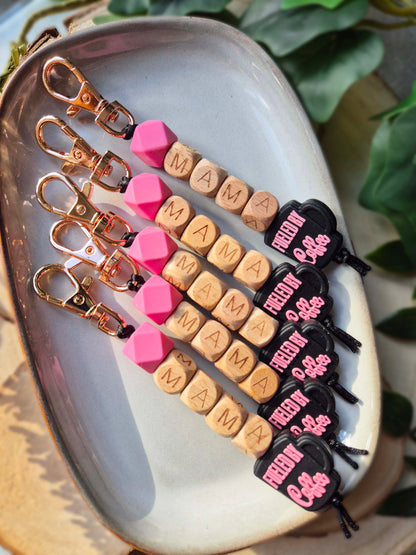 Five keychains with pink silicone beads, beech wood beads and a black and pink coffee bead.