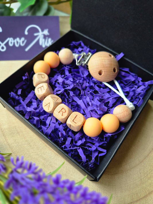 Black gift box with purple shredding holding a personalised soother clip