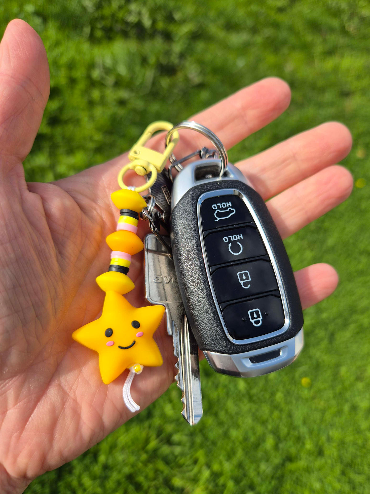 Yellow smiley star keychain clipped to car keys, held in a hand