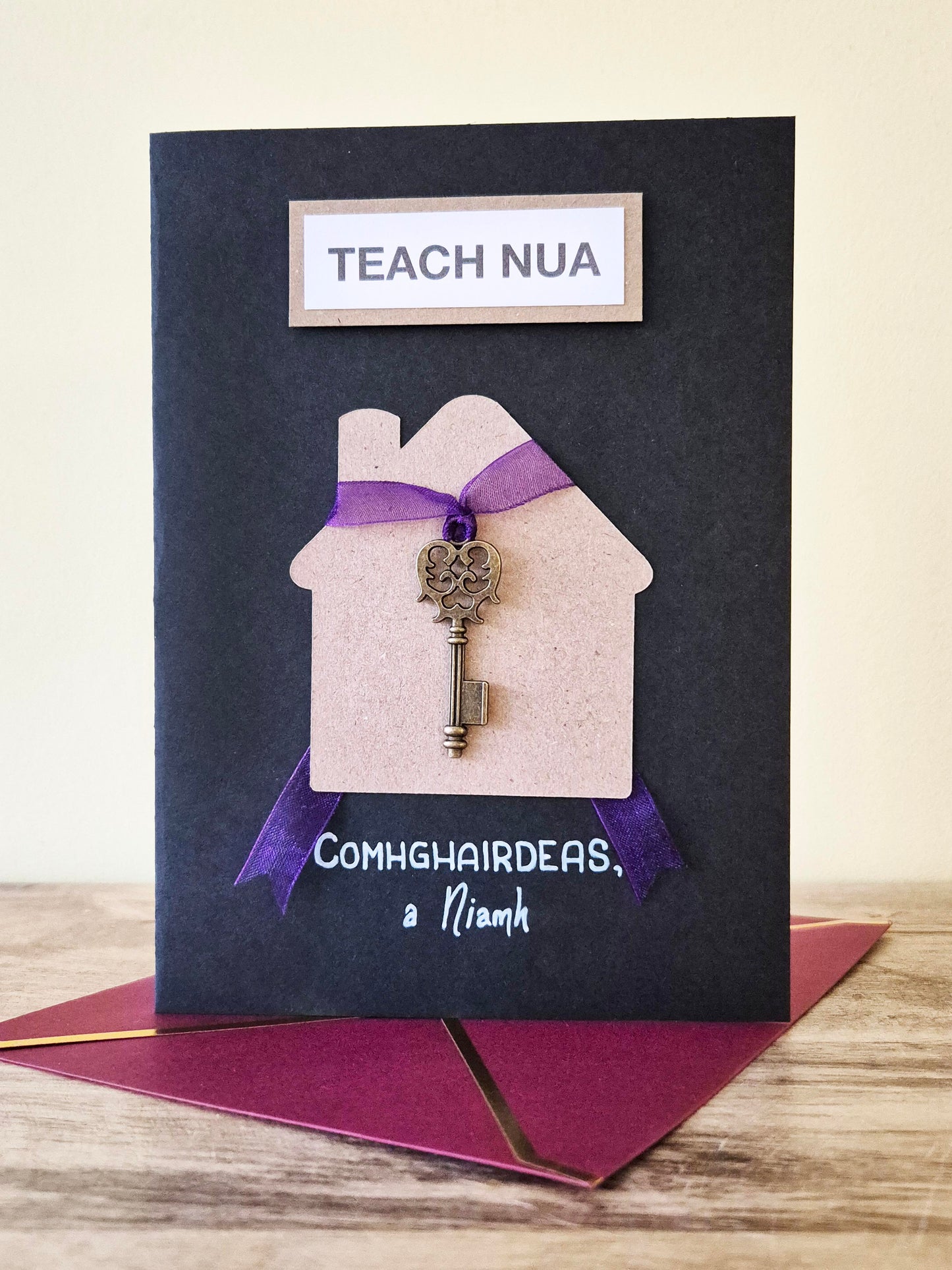 Teach Nua - Card. The Irish for New Home.  Customised with your choice of name(s). Key tied to a purple ribbon. Writing as gaeilge