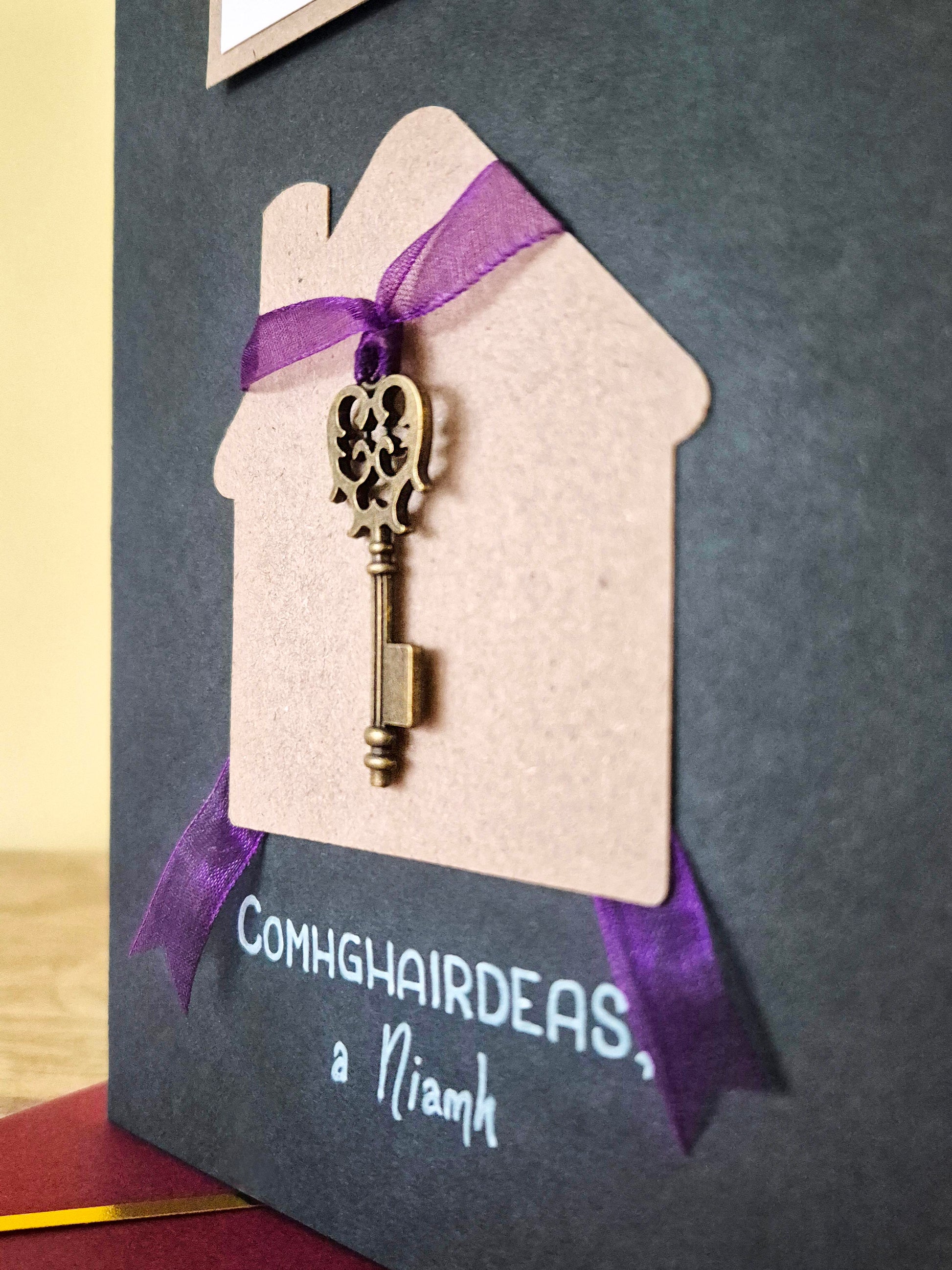 Teach Nua - Card. The Irish for New Home.  Customised with your choice of name(s). Key tied to a purple ribbon. Writing as gaeilge