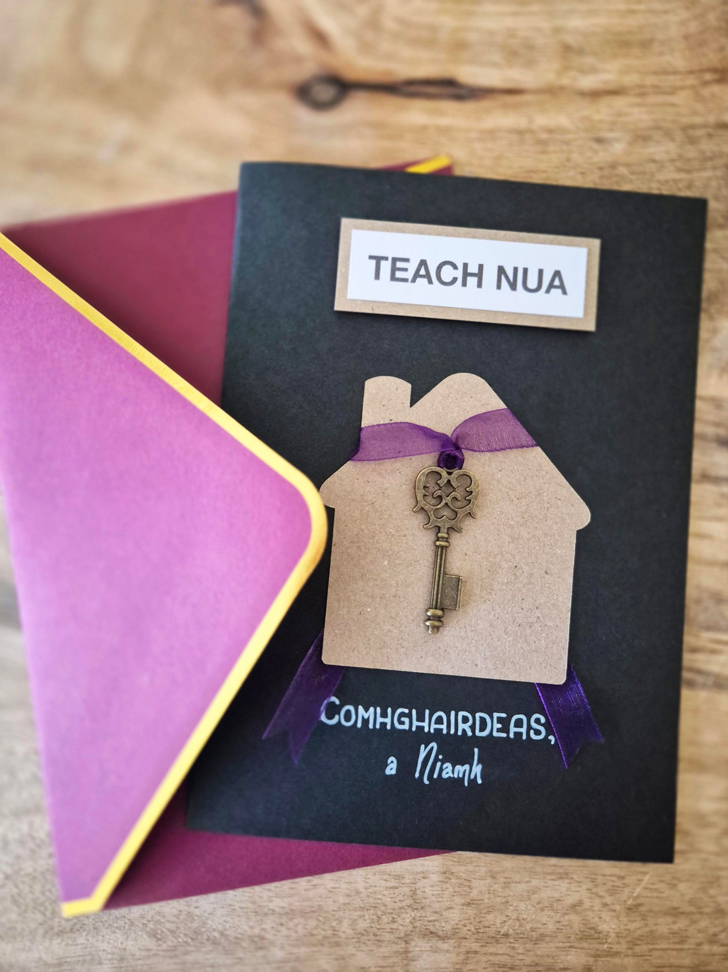Teach Nua - Card. The Irish for New Home.  Customised with your choice of name(s). Key tied to a purple ribbon. Writing as gaeilge