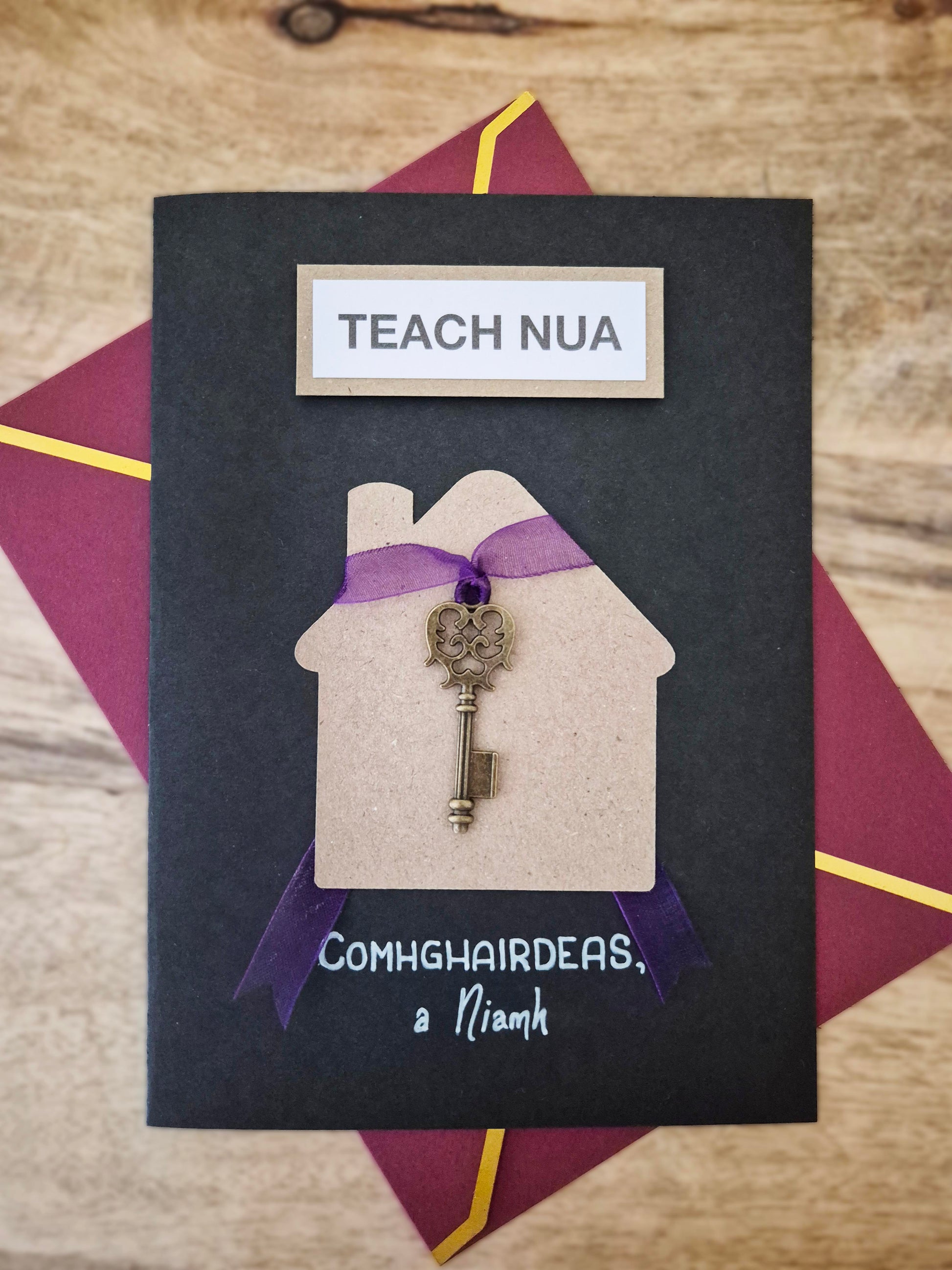 Teach Nua - Card. The Irish for New Home.  Customised with your choice of name(s). Key tied to a purple ribbon. Writing as gaeilge