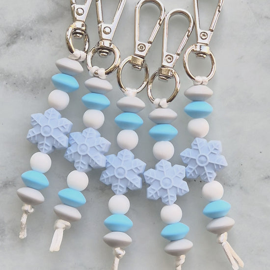Video of five Snowflake keychains made from silicone beads. Silver clips with light blue and white beads.