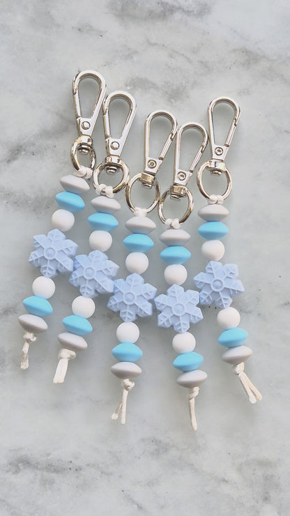 Video of five Snowflake keychains made from silicone beads. Silver clips with light blue and white beads.